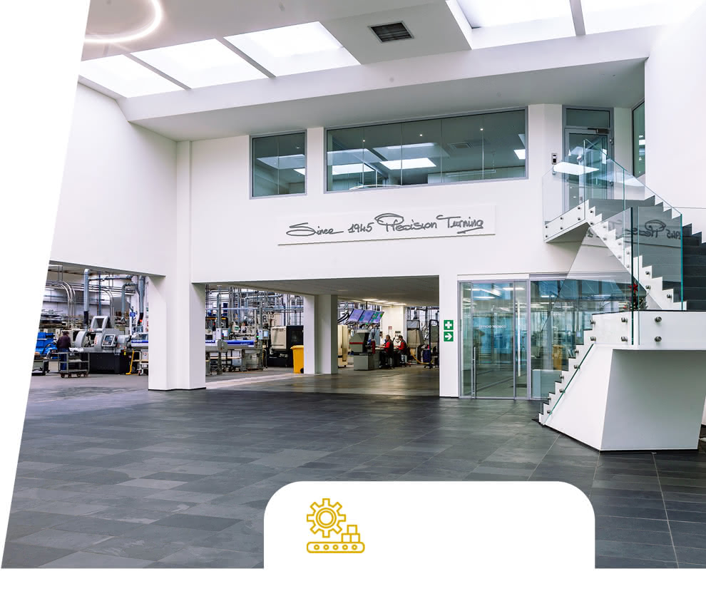 Entrance to the Eredi Baitelli production department seen from the company lobby, with glass staircase and the words “Since 1945 Precision Turning.”