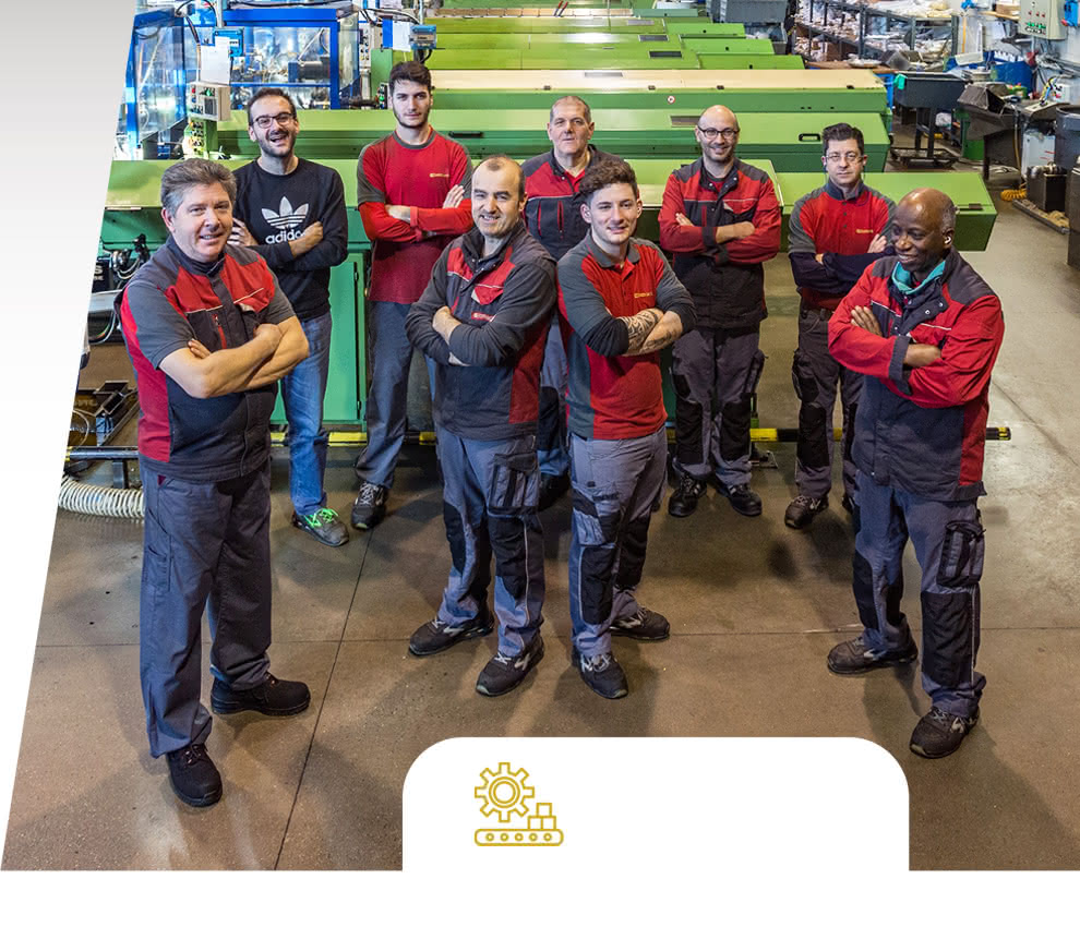 Group photo of the Eredi Baitelli team in the heart of the factory, with automatic lathes and equipment in the background.