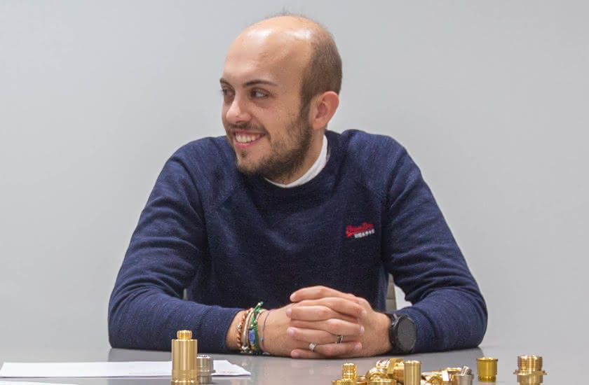 Matteo Baitelli sitting at a table with turned brass components in front of him, representing the third generation of the company.
